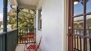 A balcony with a table and chairs, a door, and a view of trees and a building in the background.