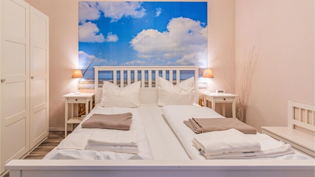 Una camera da letto con un letto, due comodini e un affresco raffigurante una spiaggia.