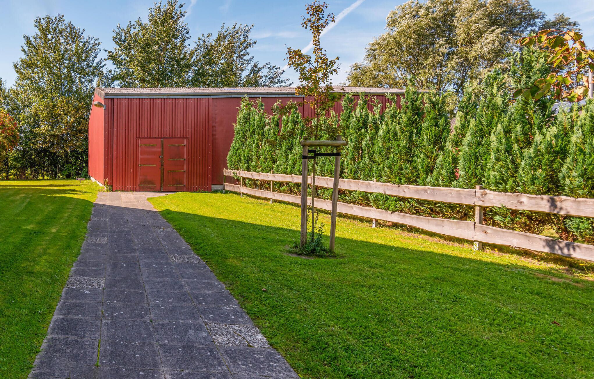 A red barn with a wooden fence and a paved path leading to it.