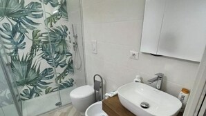 A modern bathroom with a glass shower enclosure, a white toilet, and a sink with a wooden countertop. - Delightful one-bedroom apartment in the heart of the historic Gaetano center. A stone's throw from the sea (Gaeta)