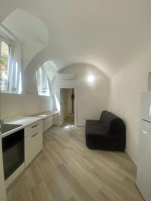 A compact kitchen with a built-in oven, a black sofa, and a window providing natural light.