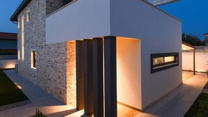 Una casa moderna con fachada de piedra, techo plano y una entrada bien iluminada.