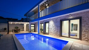 Una casa moderna con piscina, paredes de piedra y grandes puertas correderas de cristal que dan a un dormitorio.