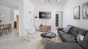 A modern living room with a grey sofa, a white rocking chair, a dining area with a wooden table and chairs, a black coffee table with books, and a colorful cabinet. - Gorgeous home in Zadar (Zadar)