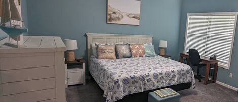 A bedroom with a bed, nightstands, a desk, a chair, a ceiling fan, and a window with blinds.