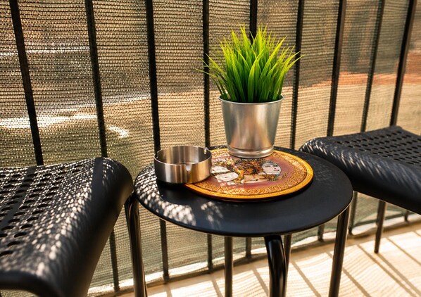 A small round table with a metal ashtray, a potted plant, and a decorative coaster with a face design.