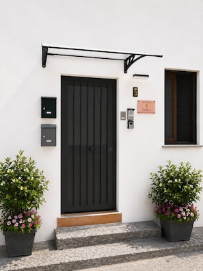 Una porta nera con una cassetta delle lettere, una targa e una finestra su un muro bianco.