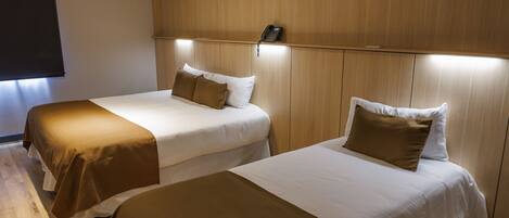 A hotel room with two beds, wooden flooring, and a ceiling light.