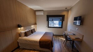 A bedroom with a bed, bedside table, and a desk with a chair. There is a window with a view of the outside. - Fuente Mayor Hotel Terminal (Mendoza)
