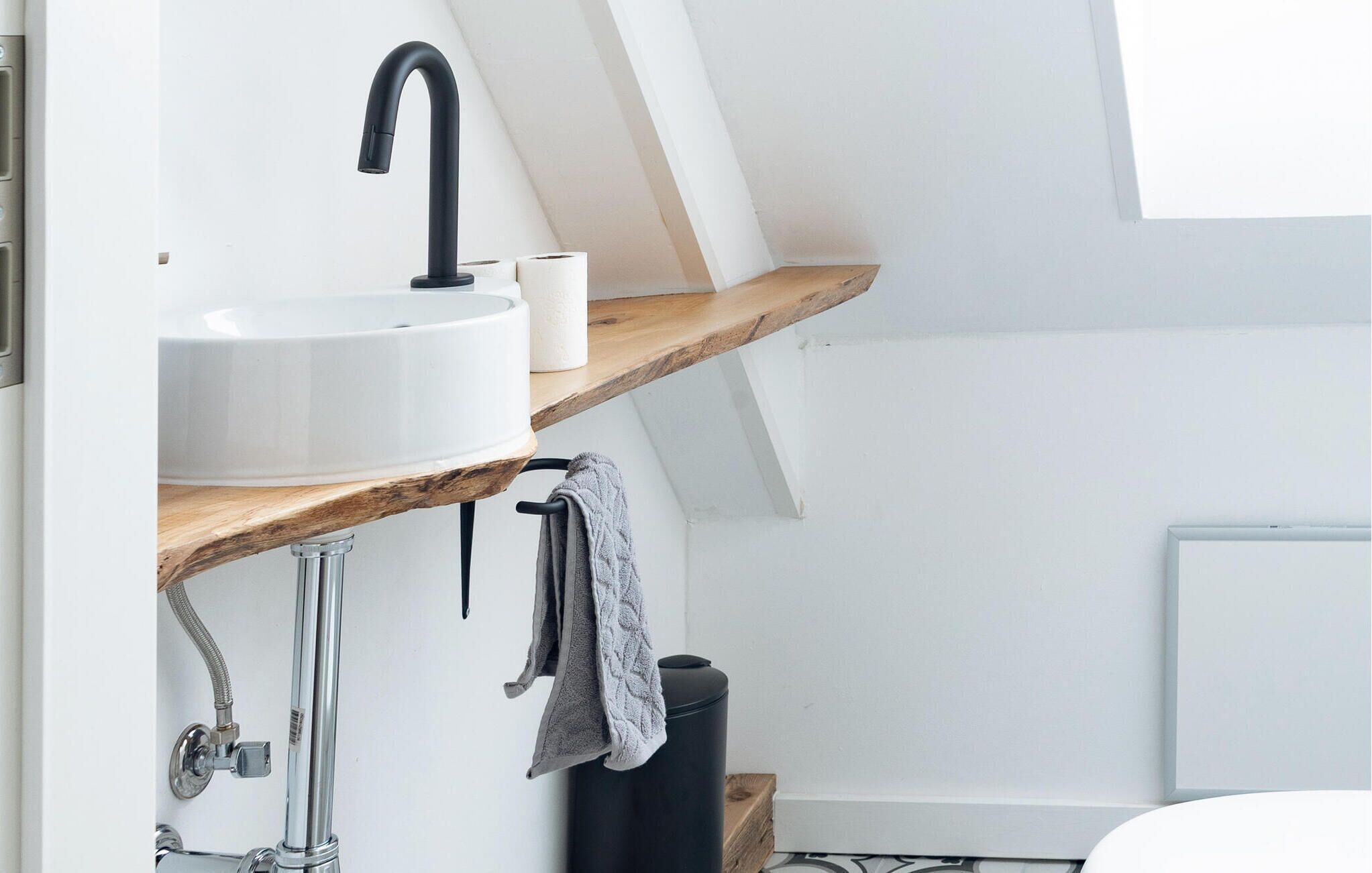 A modern bathroom with a white sink, black faucet, and wooden shelves.