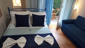 A neatly made bed with pillows, a blue headboard, and a blue sofa in a room with wooden flooring. - Comfortable, friendly, fully equipped apartment (Athina)