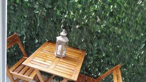 A wooden table and chairs set on a balcony with a green hedge backdrop. - Comfortable, friendly, fully equipped apartment (Athina)