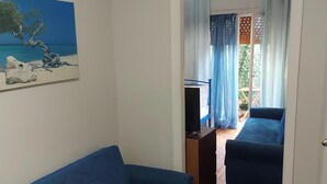 A room with a blue sofa, a painting of a beach scene, a television, and a view of an outdoor balcony with a blue sofa. - Comfortable, friendly, fully equipped apartment (Athina)