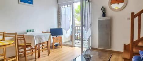 A dining area with wooden chairs and a table, a television, and a view of the outdoors through a glass door.
