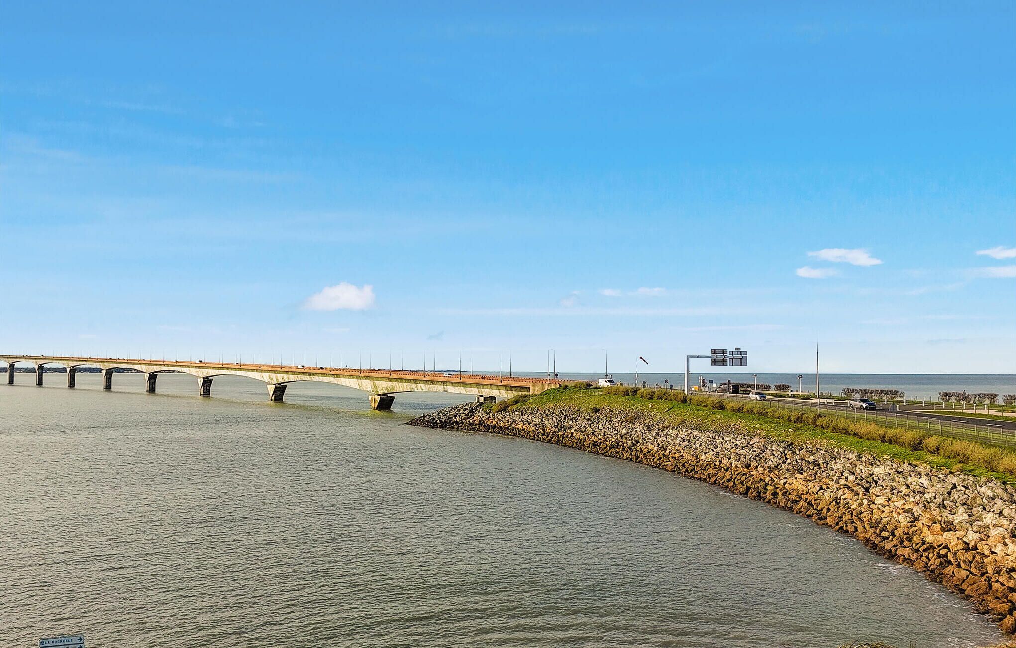 A coastal road with a bridge, a rocky embankment, and a clear sky.