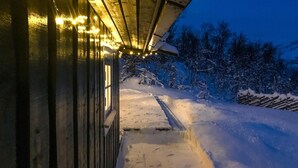 Ein verschneiter Pfad führt zu einem Gebäude mit einem geneigten Dach und Lichterketten.