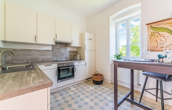 Eine moderne Küche mit weißen Schränken, einem eingebauten Backofen und einem großen Fenster, das für natürliches Licht sorgt.