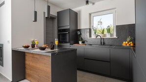 A modern kitchen with dark cabinetry, a wooden island, a built-in oven, and a window with plants. - Luxurious home in Labin with private swimming pool, can be inside or outside (Labin)