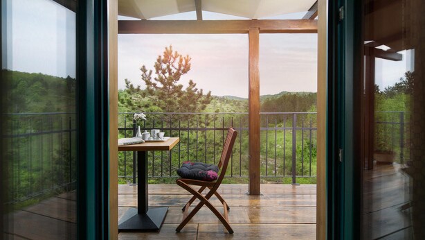 Un balcone con un tavolo di legno, una sedia e vista su un paesaggio boschivo.