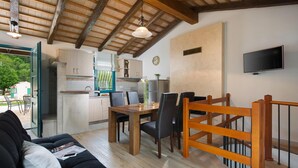 Una cucina moderna con travi in legno, un'area pranzo con tavolo e sedie in legno, un divano nero e un televisore montato a parete.