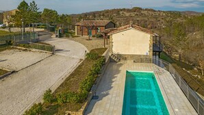 Una piscina con solarium in pietra, un piccolo edificio con tetto in tegole e un paesaggio collinare sullo sfondo.