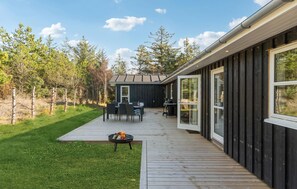 Une terrasse extérieure moderne dotée d’un espace repas, d’un barbecue et offrant une vue sur une zone boisée.