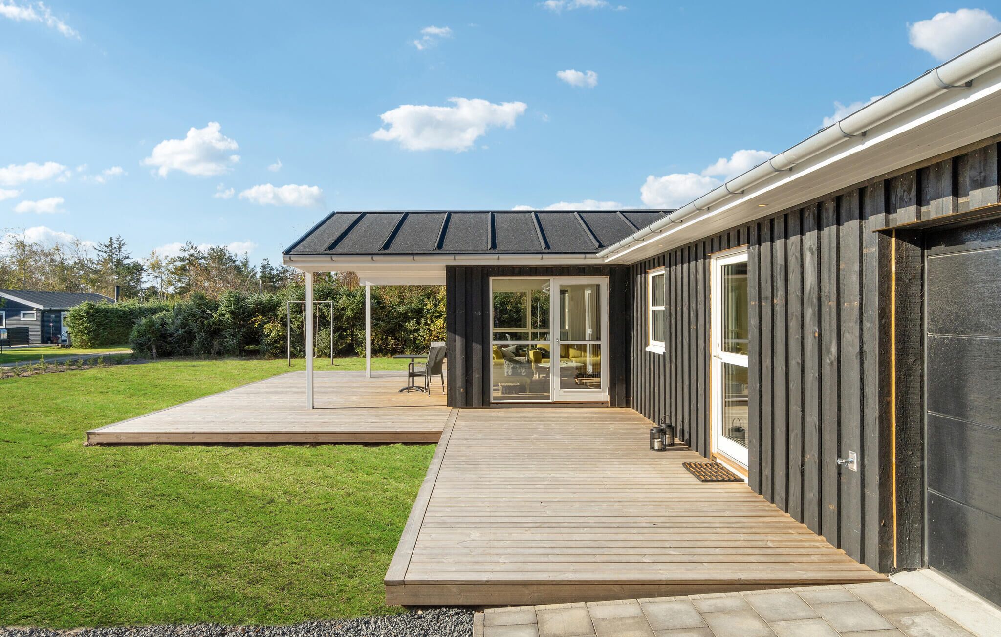 A modern house with a covered patio, a wooden deck, and a large sliding glass door leading to an outdoor seating area.