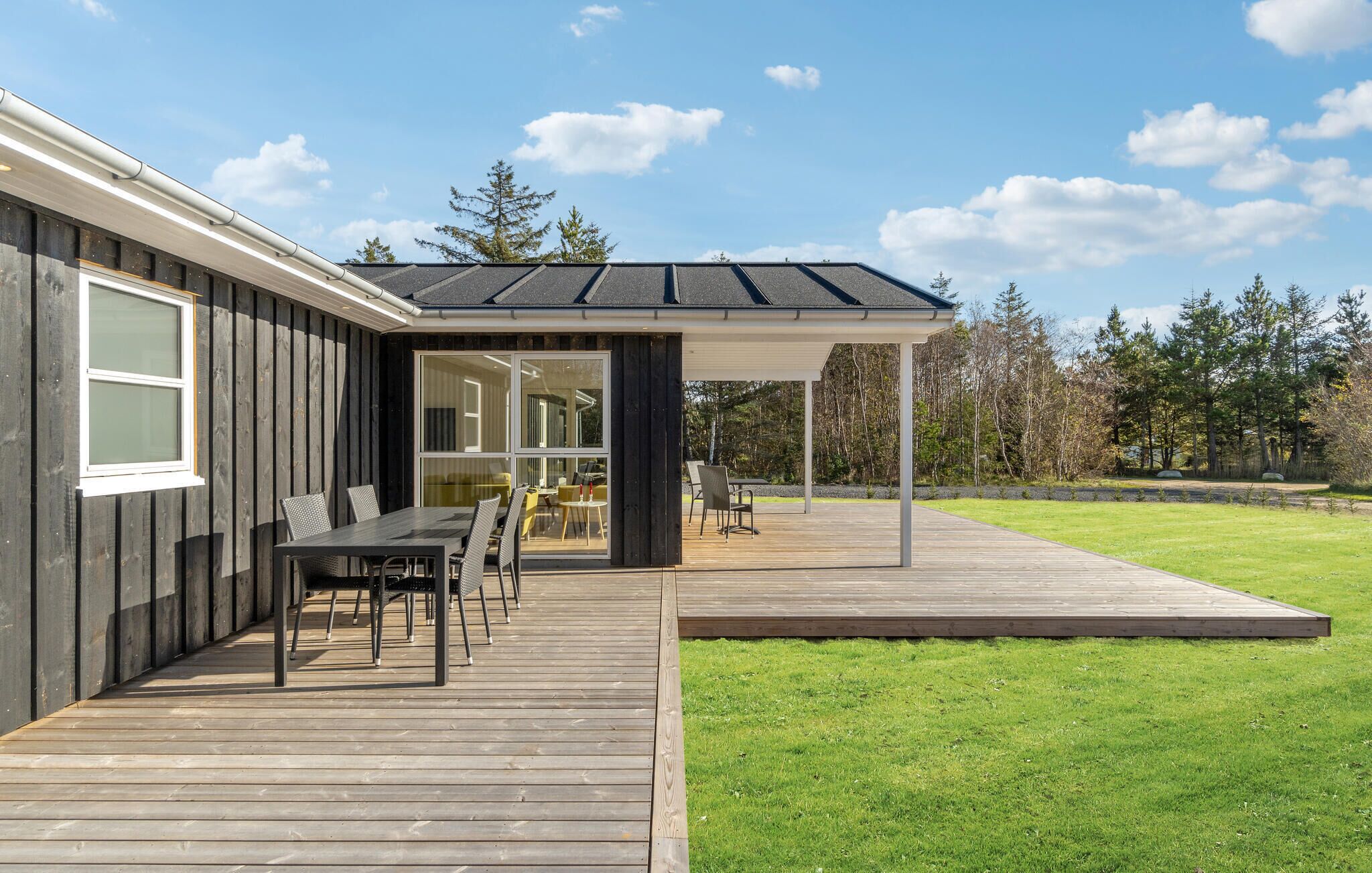 A modern house with a deck, outdoor seating, and a covered patio area.