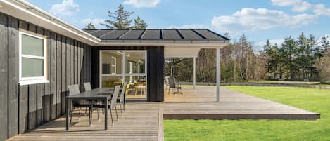 A modern house with a deck, outdoor seating, and a covered patio area.
