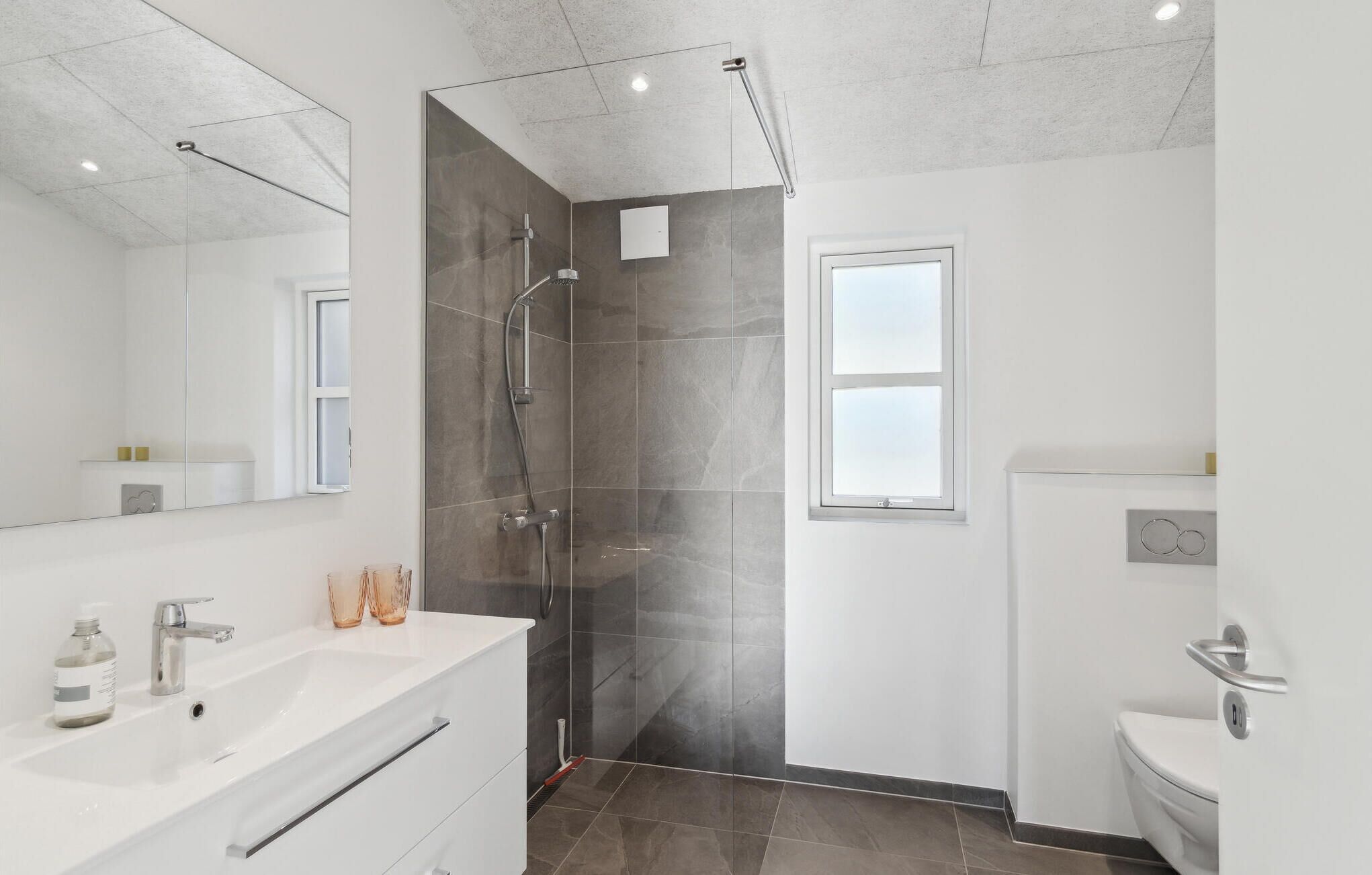 A modern bathroom with a glass-enclosed shower, a large mirror, and a white sink.