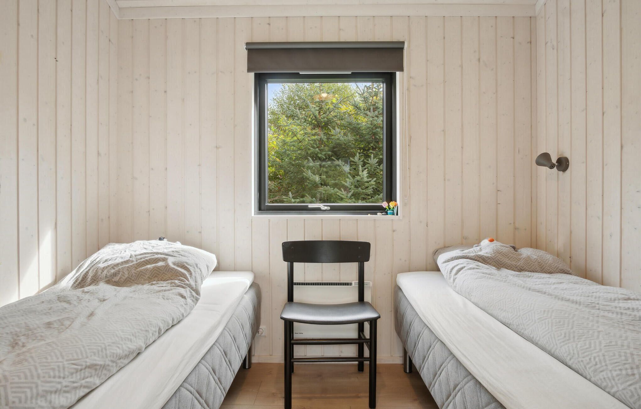 Une petite pièce avec deux lits, une chaise et une fenêtre donnant sur des arbres.