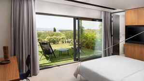 Un dormitorio moderno con un amplio ventanal corredero que da a un balcón con vistas a un paisaje verde y montañas distantes.