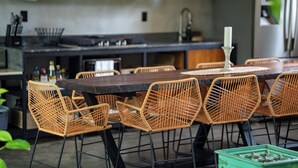 A dining area with a dark wooden table surrounded by wicker chairs, a white candle centerpiece, and a green crate with decorative items. - Suwa Villa Arenal | Amazing Location in La Fortuna (la fortuna, calle 468, avenida 335)