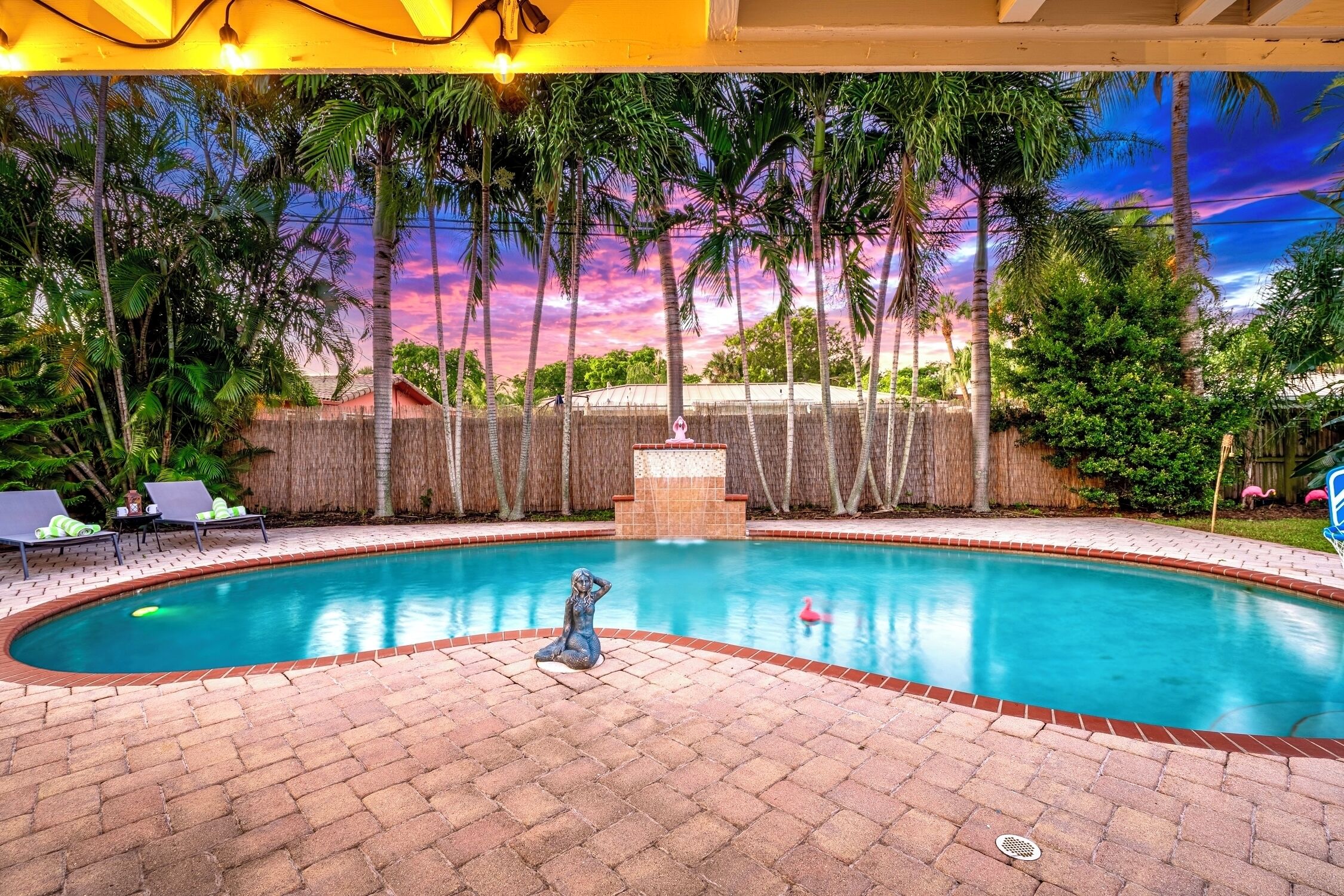 A swimming pool with a statue, surrounded by palm trees and a brick patio.