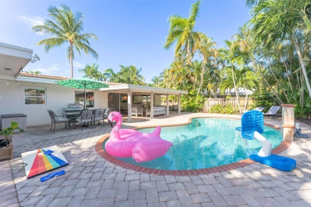 Ein Swimmingpool mit einem Flamingo-Schwimmspielzeug, einer überdachten Terrasse und Palmen im Hintergrund.