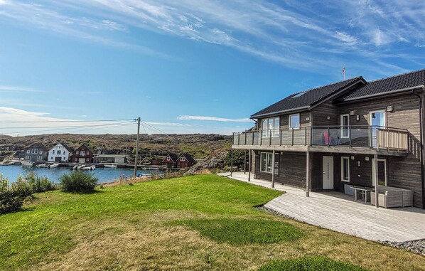 A two-story house with a balcony overlooking a body of water and a rocky landscape.