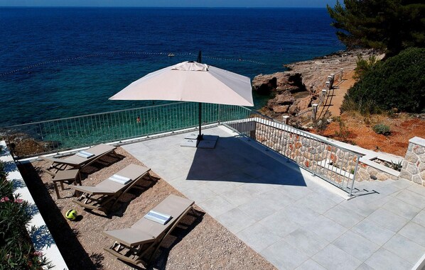 Un patio con poltrone relax e un ombrellone di grandi dimensioni con vista sul mare.