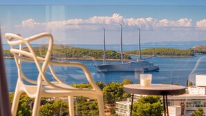 Un balcón con vista a un yate anclado cerca de la costa, rodeado de vegetación y edificios.