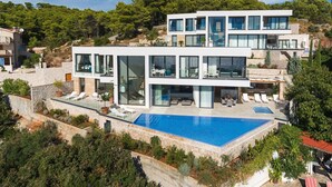 Una casa moderna de dos pisos con una gran piscina, varios balcones y zonas de estar al aire libre.