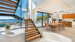 Un interior moderno con una escalera de cristal, un comedor con vistas y una cocina con armarios de madera.