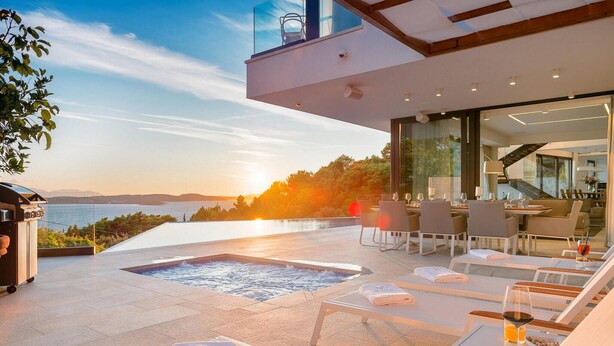 Una terraza moderna al aire libre con jacuzzi, zona de estar y vistas al mar al atardecer.