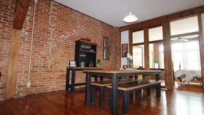 Ein Zimmer mit freiliegenden Backsteinwänden, Holzbalken, einem großen Tisch mit Bänken und einer hängenden Leuchte.