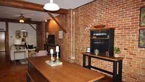 Ein Essbereich mit Holztisch, Bänken, einer Ziegelwand und einer kleinen Bar mit Gläsern.