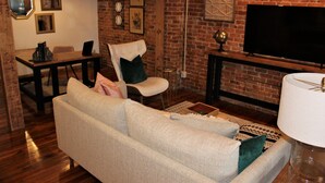 Ein Wohnzimmer mit Backsteinwand, einer Couch, einem Fernseher und einem Essbereich.