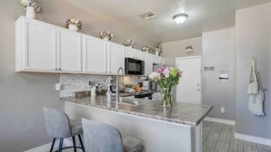 A modern kitchen with white cabinets, a granite countertop, and two bar stools. - Sandstone Bliss - 3 bed, 2.5 Bath Cozy Home! (Mesa)