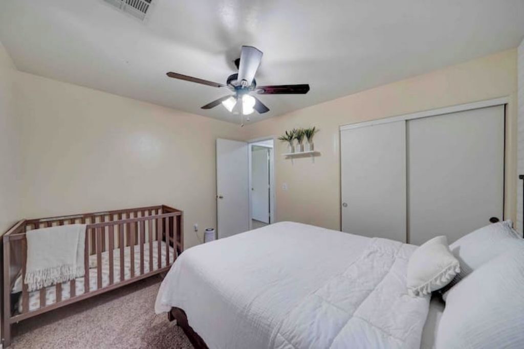 A bedroom with a crib, a bed, a ceiling fan, and a closet.