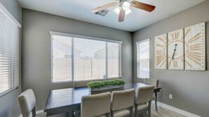 A dining area with a dark wooden table, four chairs, a ceiling fan, and large windows with blinds. - Sandstone Bliss - 3 bed, 2.5 Bath Cozy Home! (Mesa)