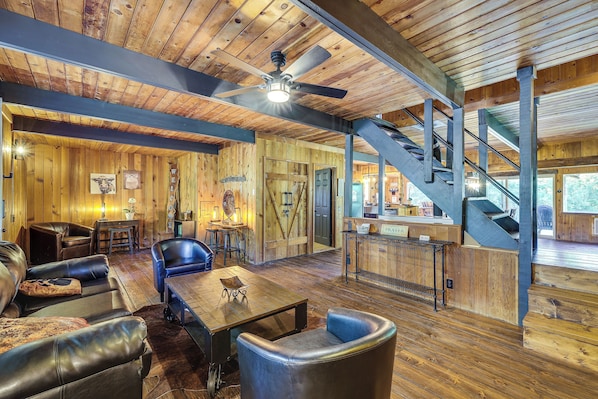 A spacious room with a wooden ceiling, a dining table, leather chairs, and a staircase leading to another level.