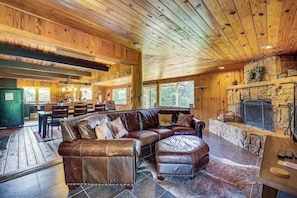 A spacious living area with a leather sectional sofa, a stone fireplace, and a dining area with wooden tables and chairs.
