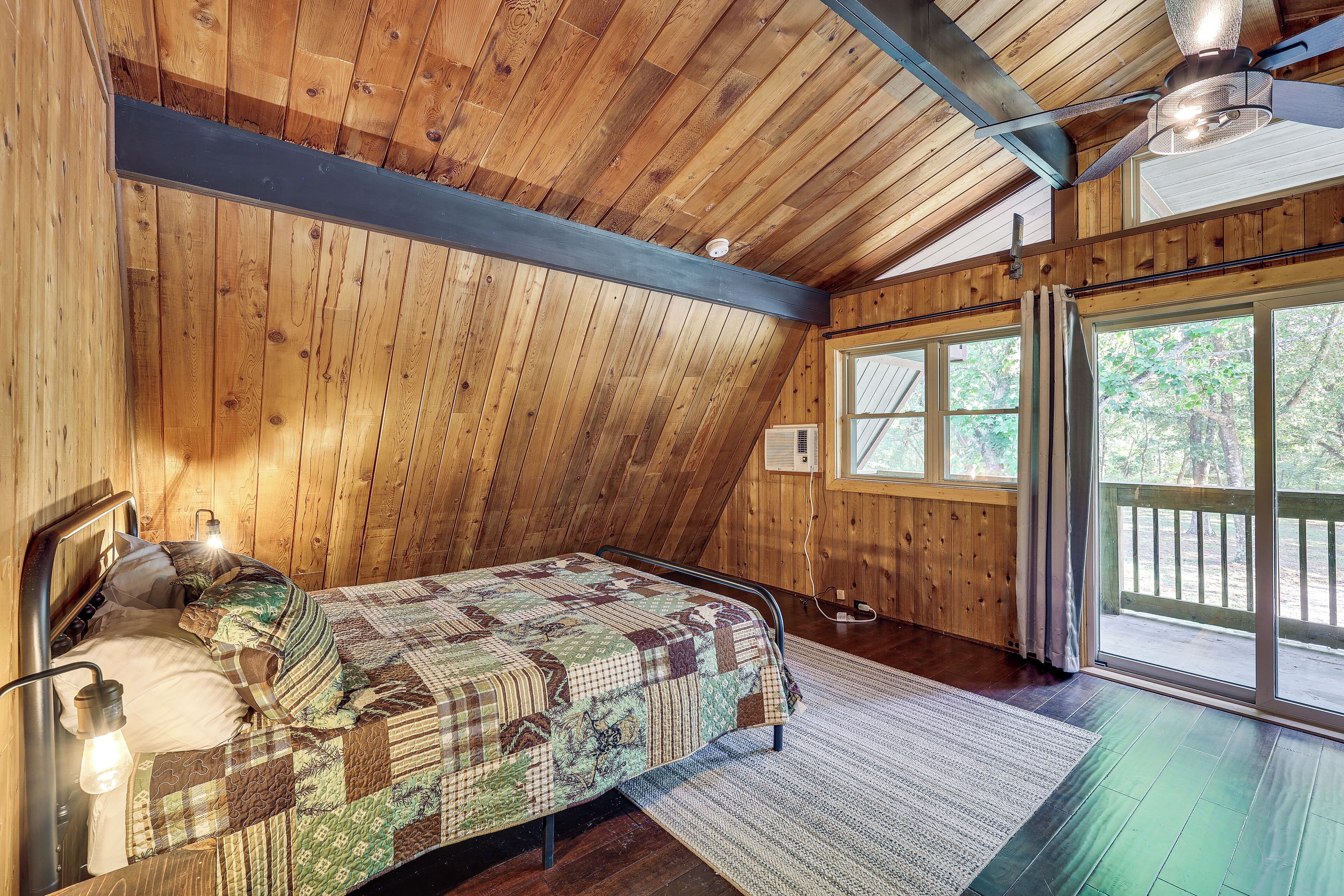 A single bed with a quilt, a ceiling fan, and a window with a view of trees.
